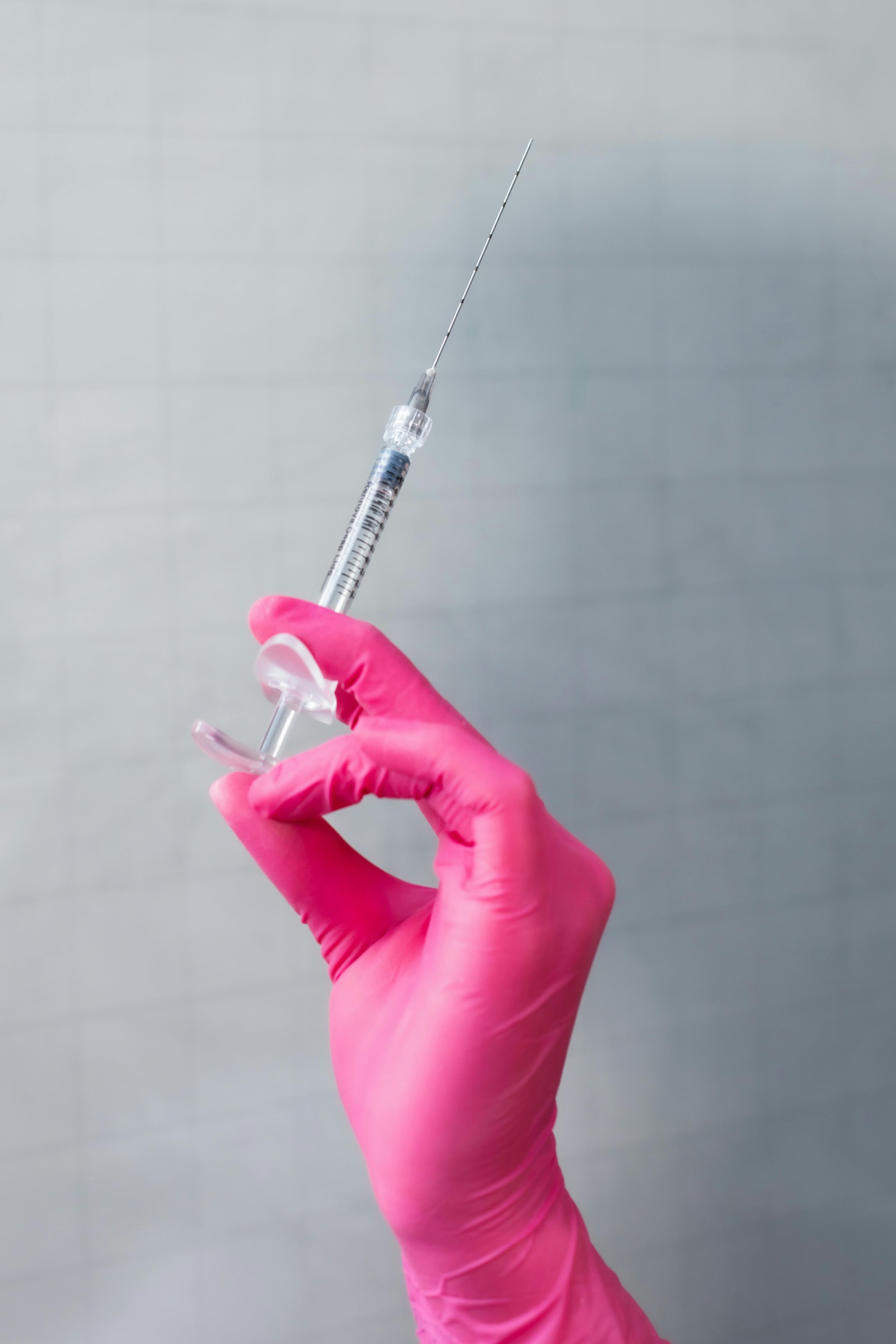 A person wearing a pink glove is holding a syringe, ready for a medical procedure or vaccination.
