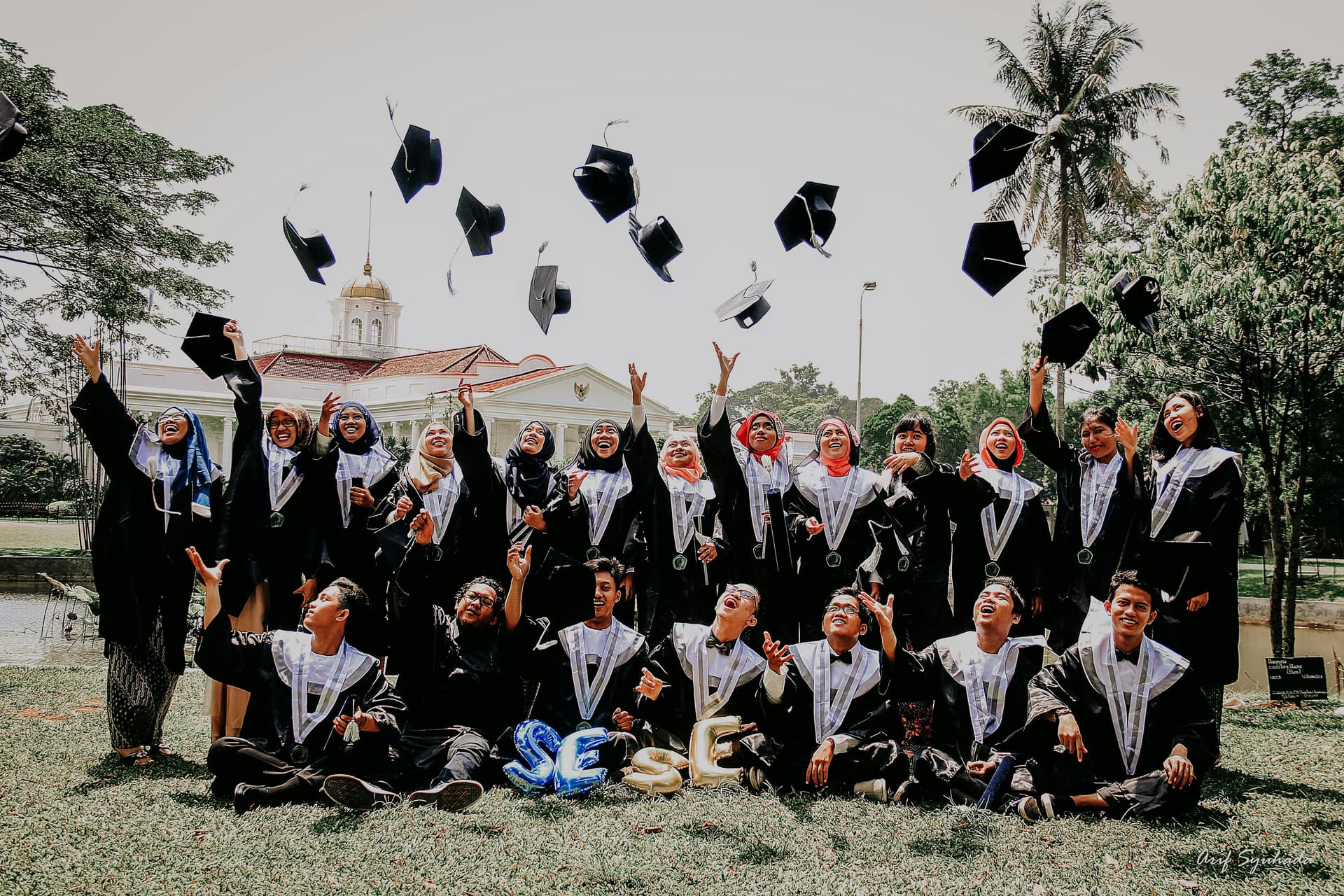 A diverse group of graduates wearing caps and gowns, celebrating their academic achievements together outdoors.